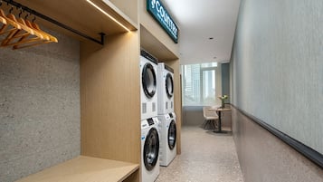 A hotel laundry room with two stacked washing machines, a wooden bench, and a sign that reads 'COUNTRY'.