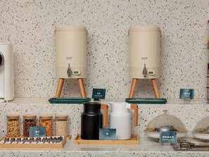 Una kitchenette con dos máquinas de café, una zona de té y varios recipientes de comida.