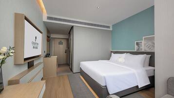 Une chambre d’hôtel équipée d’un lit, d’un bureau, d’une chaise, d’une télévision et d’une porte donnant accès à une salle de bain.