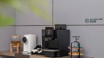 A coffee machine, a tea dispenser, and a fruit display on a counter.