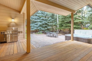 A covered outdoor area with a stainless steel grill, a hot tub, and a seating area with a table and chairs. - Spacious Warm Springs Home | Hot Tub + Bunk Room (Ketchum)
