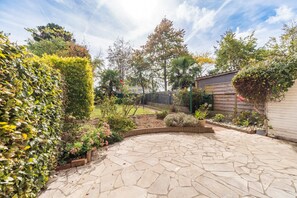 Ein Garten mit einer Steinterrasse, verschiedenen Pflanzen und einem Holzzaun.