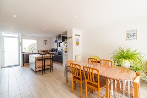 Una cocina moderna con una isla central, un comedor con una mesa redonda y sillas, y una planta grande en maceta.