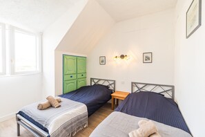 Ein Zimmer mit zwei Betten, einem grünen Kleiderschrank, einem kleinen Tisch und einer Wandleuchte.