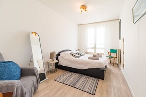 A modern bedroom with a bed, a bedside table, a chair, a mirror, and a window. - 3-bedroom house in Saint-Brieuc, comfort and quiet (Saint-Brieuc)