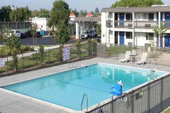 Piscina rectangular con escalera metálica, rodeada por una cerca y algunas sillas de descanso.