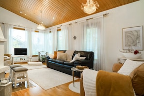 Ein modernes Wohnzimmer mit einer schwarzen Ledersofa, weißen Kissen, einem Glastisch und einer Holzbalkendecke.