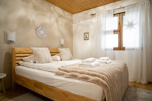 Ein Schlafzimmer mit einem hölzernen Bett, weißer Bettwäsche, einem flauschigen Teppich, einer Wanddekoration und einem Fenster mit Vorhängen.