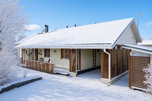 Ein mit Schnee bedecktes Gebäude mit geneigtem Dach, Holzhörnern und einer kleinen Veranda mit Sitzgelegenheit.