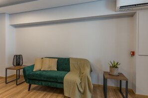 Ein Zimmer mit einem grünen Sofa, zwei Beistelltischen, einer Topfpflanze und einer Klimaanlage an der Wand.