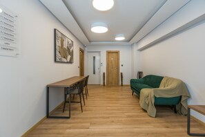 Ein Hotelzimmer mit Holzboden, einem Esstisch mit Stühlen, einem grünen Sofa und einem Gemälde an der Wand.