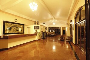 A hotel reception area with a reception desk, a large mirror, and a chandelier. - Ushaascot (Matheran)