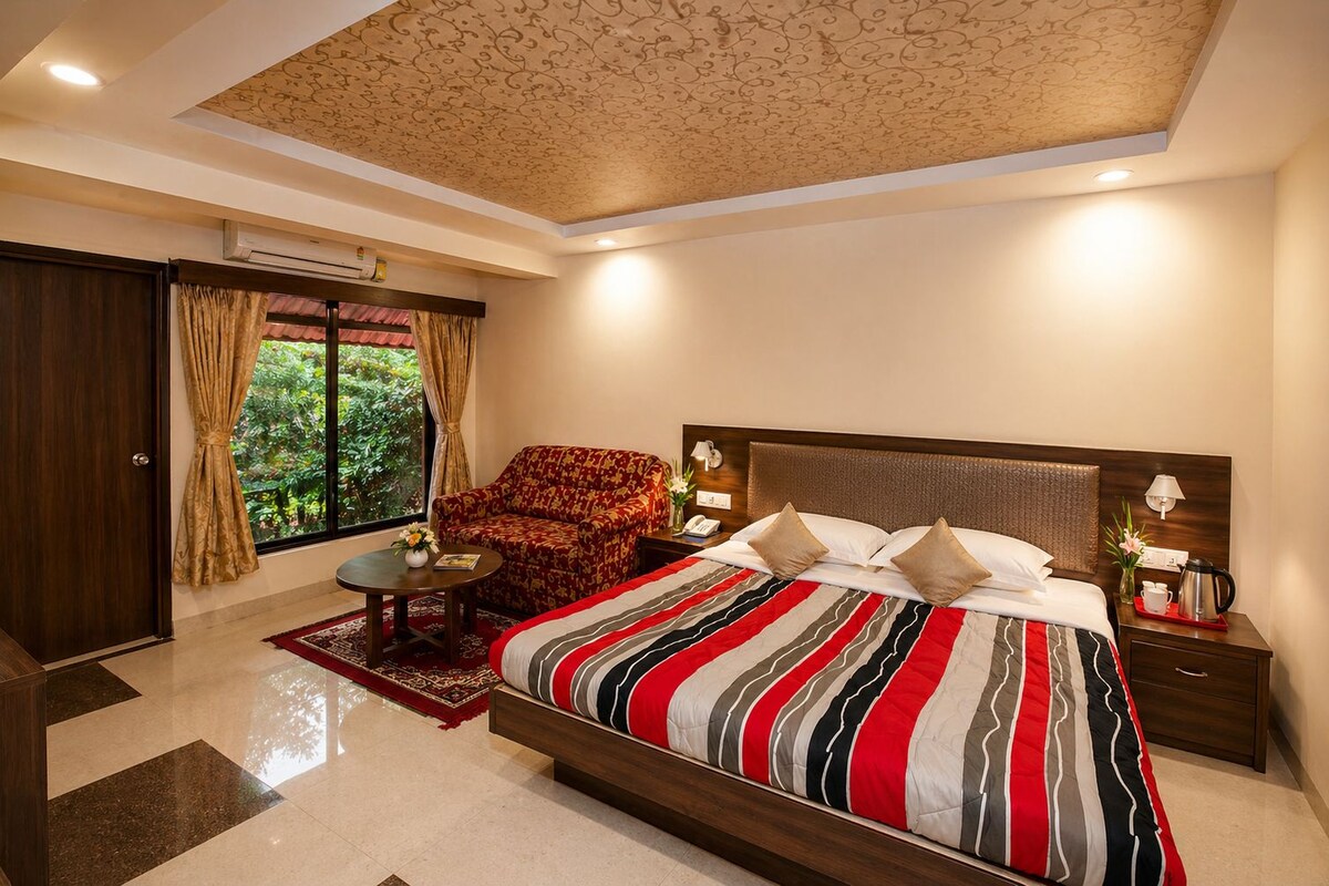 A hotel room with a large bed, a sofa, a small table, and a window with curtains.