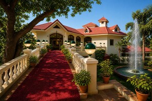 A hotel with a red-tiled roof, a red carpeted walkway, and a fountain. - Ushaascot (Matheran)
