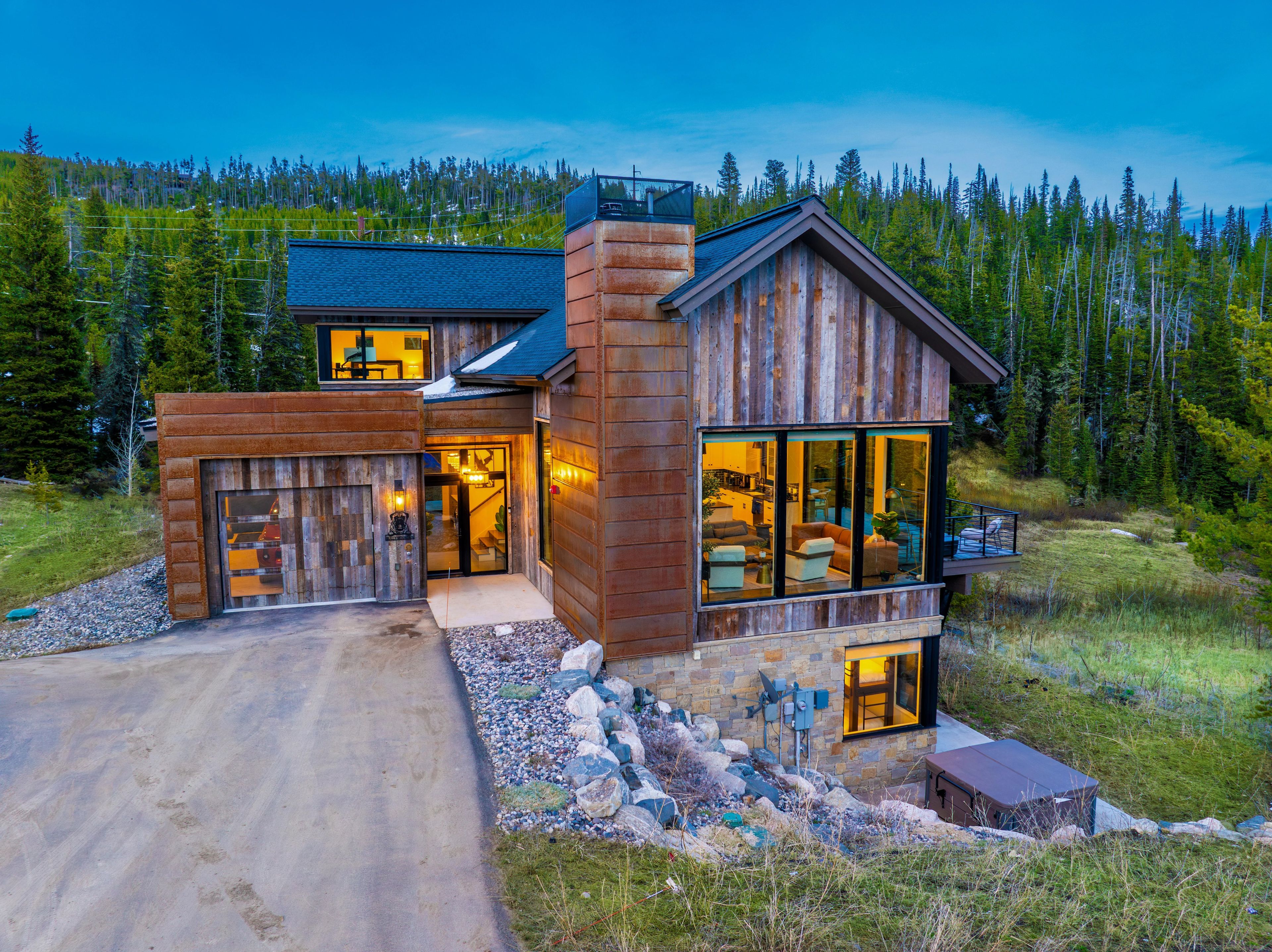 A modern log cabin with a garage, large windows, and a stone foundation.