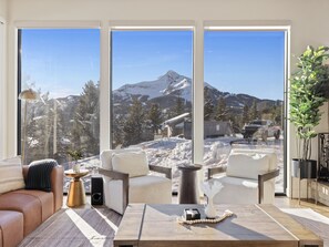 Ein modernes Wohnzimmer mit einem großen Fenster mit Blick auf eine verschneite Berglandschaft.