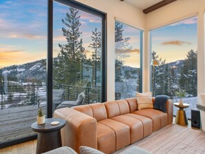 Ein modernes Wohnzimmer mit einer Ledersofa, großen Fenstern und Blick auf eine verschneite Berglandschaft.