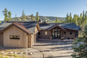 A lodge with a gravel driveway and wooden exterior, surrounded by trees and a mountain backdrop. - New! Entire Home Big Sky Summit - Private Hot Tub with Ski-In Ski-Out Access (Big Sky)