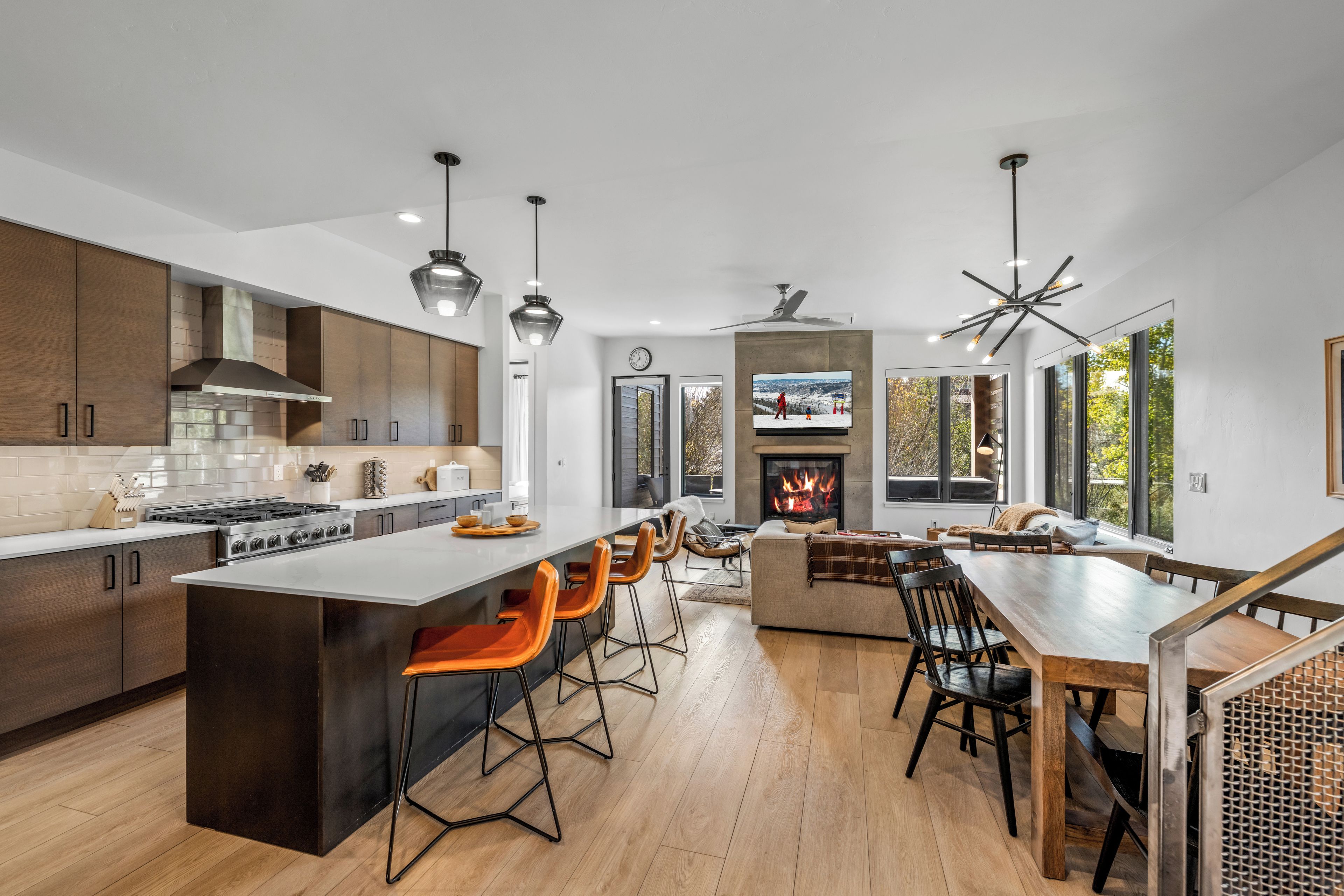 A modern kitchen with a central island, bar stools, a fireplace, and a dining area with a wooden table and chairs.