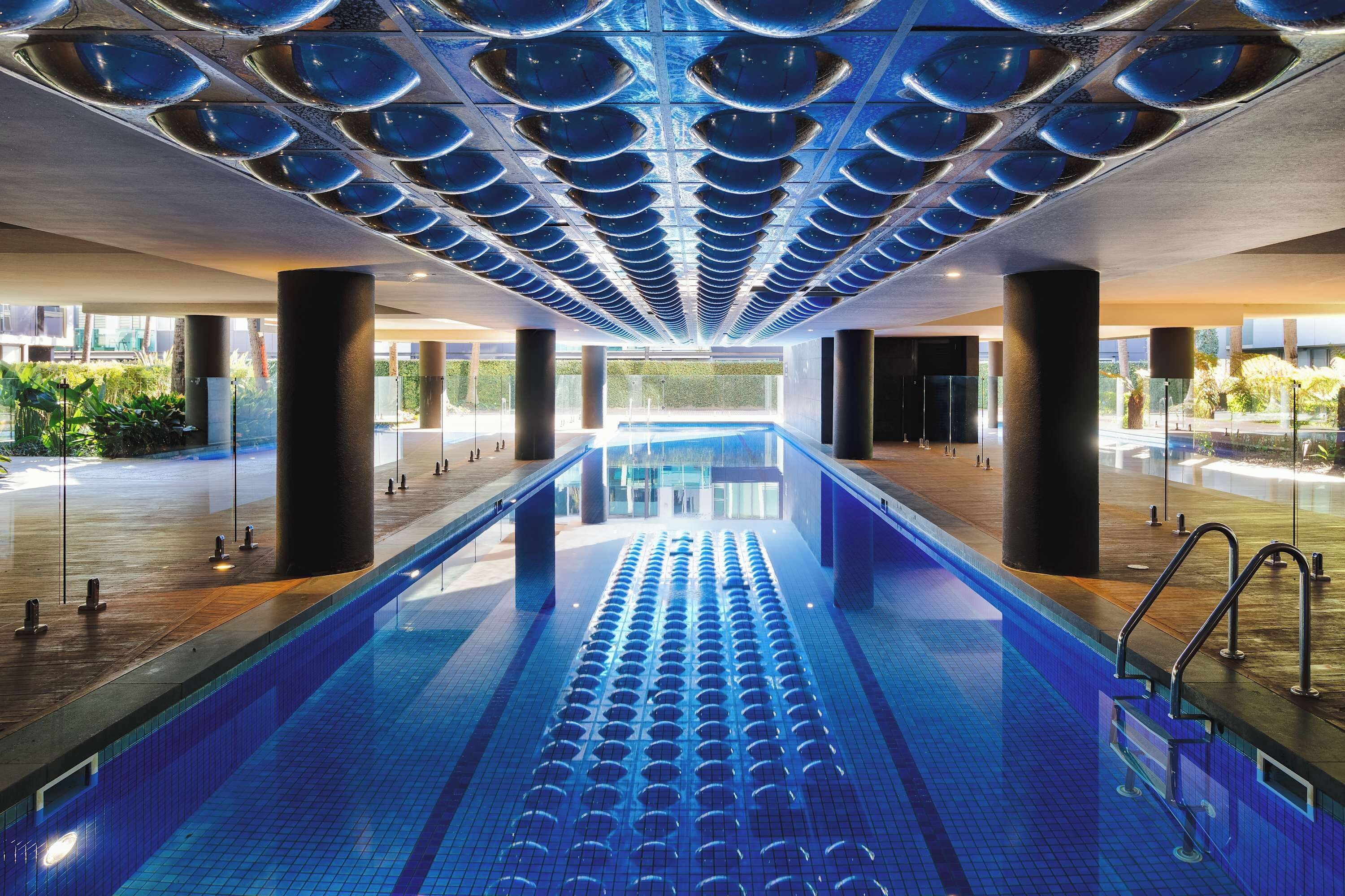 Une longue piscine intérieure au design moderne, entourée de murs de verre et soutenue par de grandes colonnes.