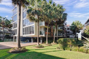 A modern building with multiple floors, large windows, and a well-maintained garden with palm trees and shrubs. - North Edit - Port Melbourne Beachside (Port Melbourne)