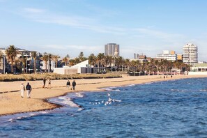 A beach with people walking, palm trees, and buildings in the background. - North Edit - Port Melbourne Beachside (Port Melbourne)