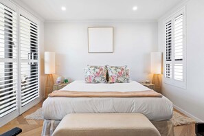 Ein Schlafzimmer mit einem großen Bett, zwei Nachttischlampen, einem gerahmten Bild an der Wand und einer Bank am Fußende des Bettes.