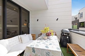 Eine Terrasse mit einem weißen Sofa, einem Tisch mit einer blumigen Tischdecke und einem Grill.