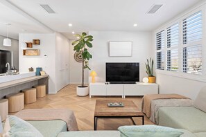 Uma sala de estar moderna com televisão de tela plana, uma planta em vaso e uma área de refeições com balcão de cozinha.