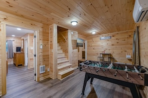 Ein Zimmer mit Holzboden, einem Kicker, einem Fernseher und einer Treppe, die zu einem anderen Raum führt.