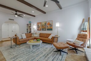 A modern living room with a brown leather sofa, a round coffee table, and a single armchair. There is a bookshelf filled with books and a globe on the wall. - Walk to Wigwam Resort! Family & Golfer’s Oasis (Litchfield Park)