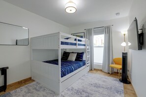 Ein Schlafraum mit Etagenbetten, einem Spiegel, einem Schreibtisch, einem Stuhl und einem an der Wand befestigten Fernseher.