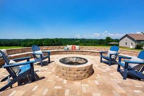 An outdoor seating area with four Adirondack chairs, a stone fire pit, and a view of a house and greenery. - Blue Ridge Views - Near Mt Airy & Wine Trail (Ararat)