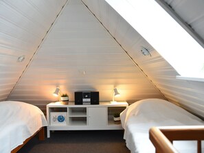 A small, triangular attic bedroom with two beds, a white wardrobe, a desk with a computer and a lamp, and a window. - Koch - From the Vines to the Wadden Sea (Wittmund)