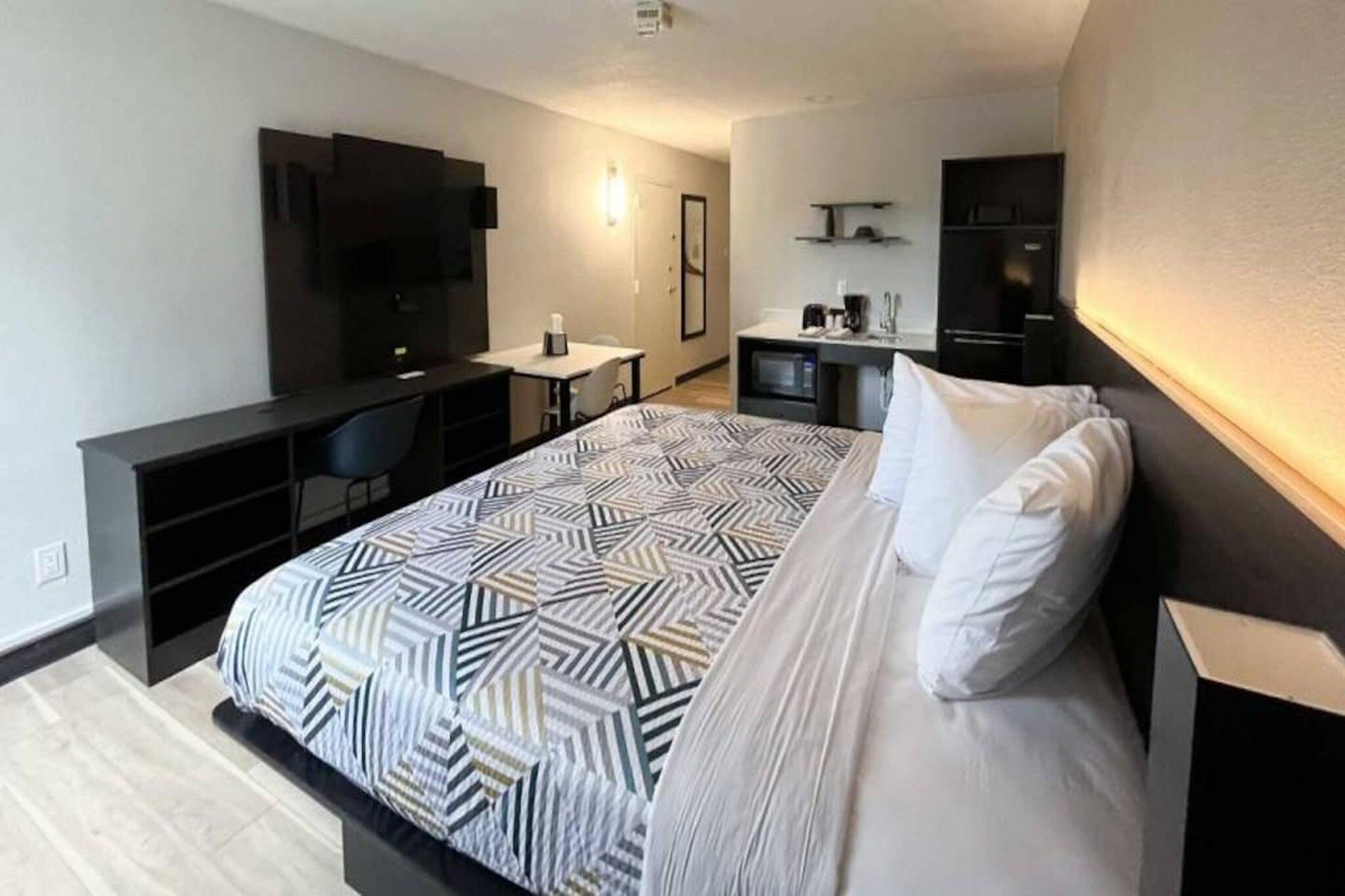 A modern hotel room with a large bed, a desk, a flat-screen TV, and a minibar.