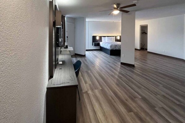 Una habitación amplia con piso de madera, una cama, un escritorio y un ventilador de techo.