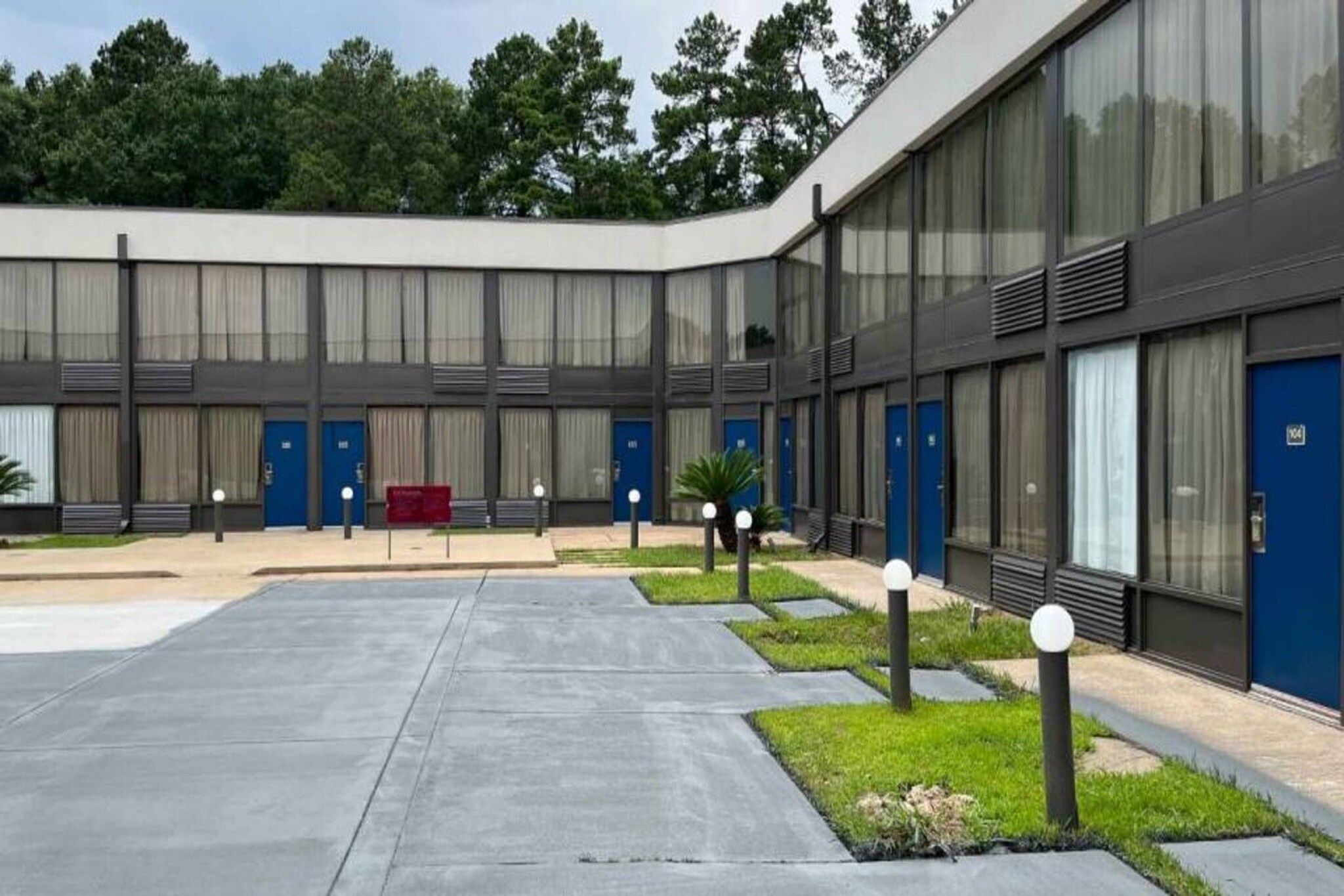 Un bâtiment moderne doté d’une cour intérieure, où l’on trouve une série de portes bleues, un banc rouge et de petits arbres.