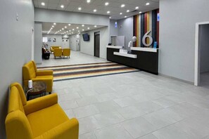 Un vestíbulo moderno con una mesa de recepción, una zona de estar amarilla y una alfombra a rayas.