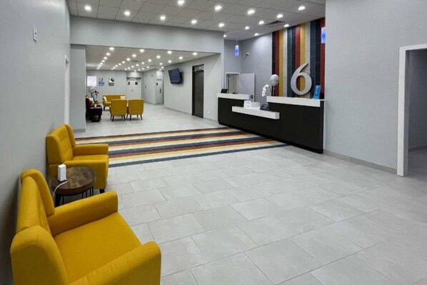 Un vestíbulo moderno con una mesa de recepción, una zona de estar amarilla y una alfombra a rayas.