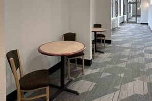 Un pasillo con piso alfombrado y dos mesas redondas con sillas.