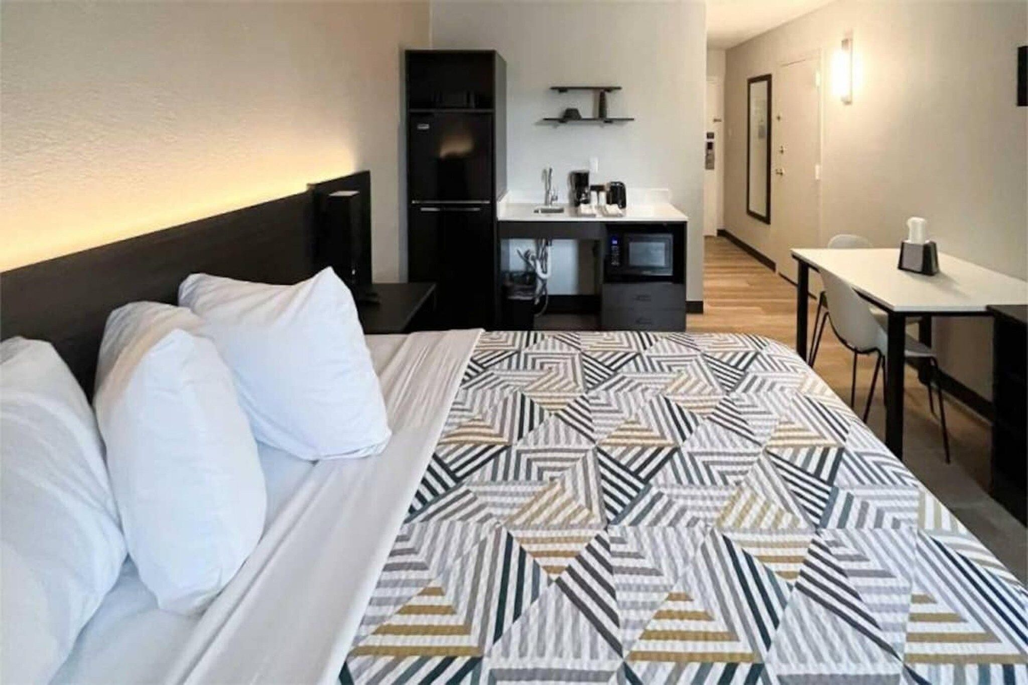 A hotel room with a bed, a desk, a wardrobe, and a kitchenette.