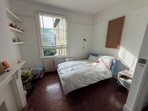 A bedroom with a bed, a radiator, a window with blinds, a shelf with items, and a door. - Characterful 1BDR Flat with Desk in Brixton Hill (London)