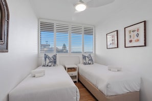 A bedroom with two beds, a nightstand, and a window with blinds. - Beachfront Apt w/ Pool & Spectacular Lake Views (Forster)