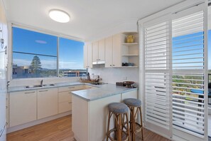 A modern kitchen with a large window, a bar area with stools, and a view of the outdoors. - Beachfront Apt w/ Pool & Spectacular Lake Views (Forster)