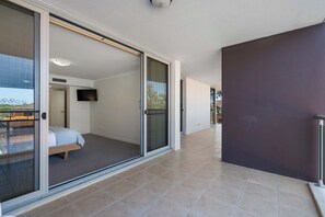 A modern hotel room with a bed, a TV, and a sliding glass door leading to a balcony. - 'Breeze' at The Crest - Spacious & Secure Parking (Forster)