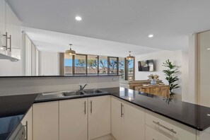 A modern kitchen with a black countertop, stainless steel sink, and white cabinets. There is a large window providing a view of the outdoors. - 'Breeze' at The Crest - Spacious & Secure Parking (Forster)