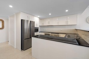 A modern kitchen with white cabinetry, stainless steel appliances, and a black countertop. - 'Breeze' at The Crest - Spacious & Secure Parking (Forster)