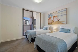Een hotelkamer met twee bedden, een schilderij aan de muur en uitzicht door een schuifdeur.