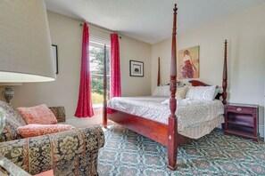 A four-poster bed with a wooden frame, a sitting area with patterned upholstery, and a large window with red curtains. - Spacious Victorian Near Holiday Valley & Town (Ellicottville)