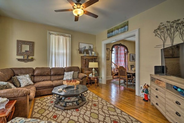 A living room with a brown leather sofa, a coffee table, a ceiling fan, and a television on a wooden cabinet. - Spacious Victorian Near Holiday Valley & Town (Ellicottville)